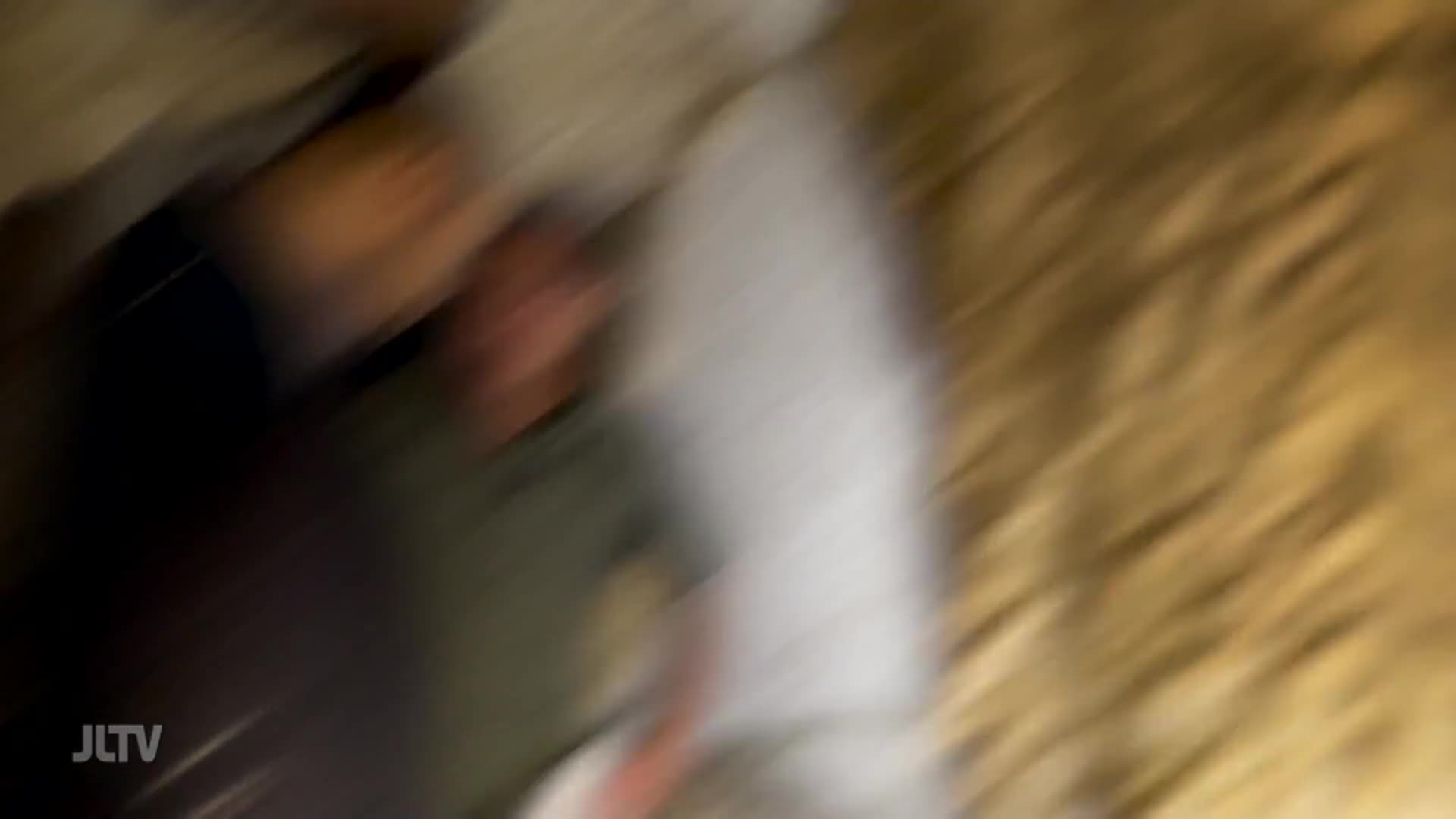 The camera is moving, capturing a quick glimpse of people. The blurred image suggests a scene from Jewish Life Television, possibly a fast-moving event.
