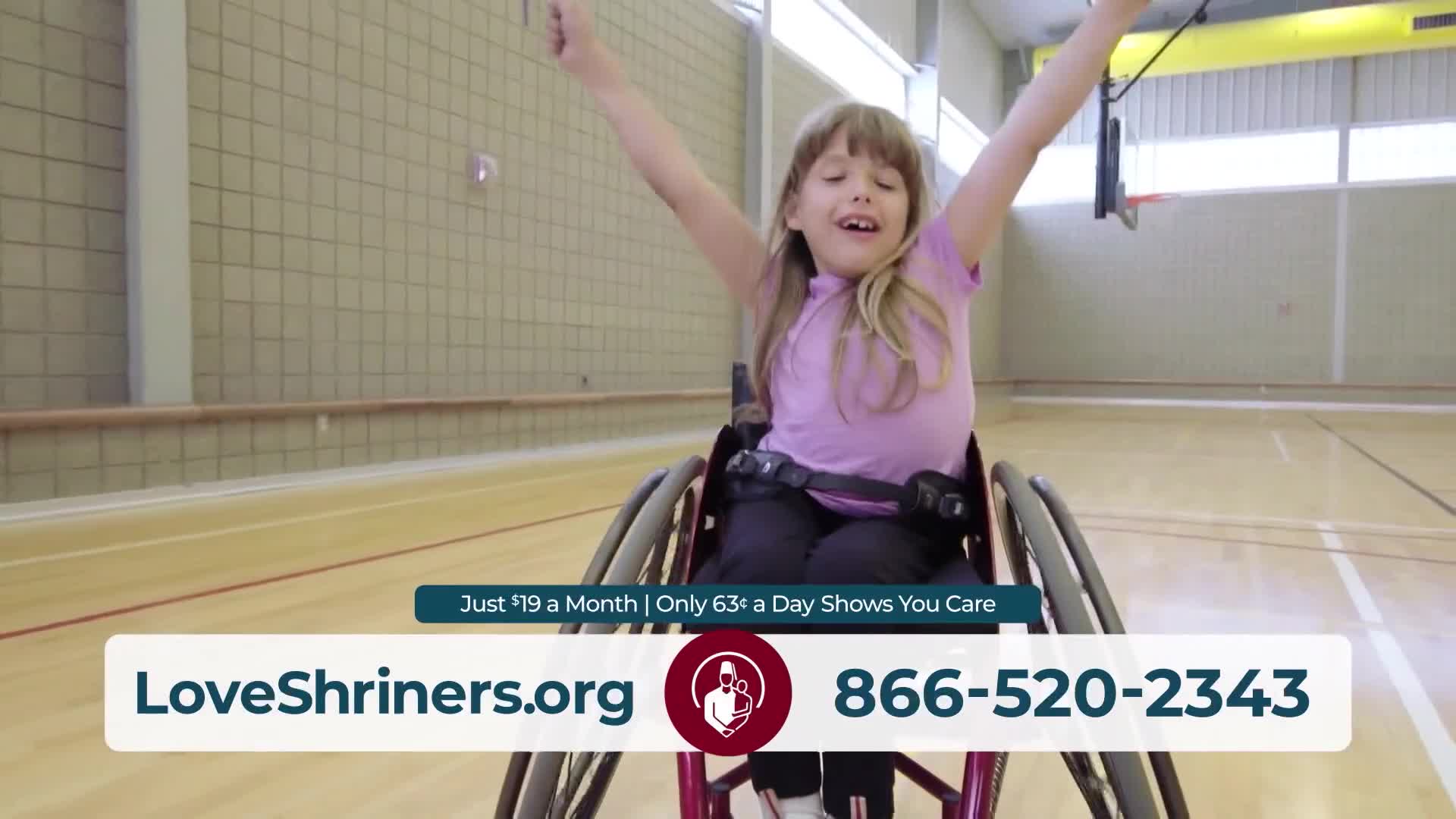 A young girl in a wheelchair raises her arms, smiling, inside a gymnasium. The scene is part of a United States public service announcement, as seen on Jewish Life Television.
