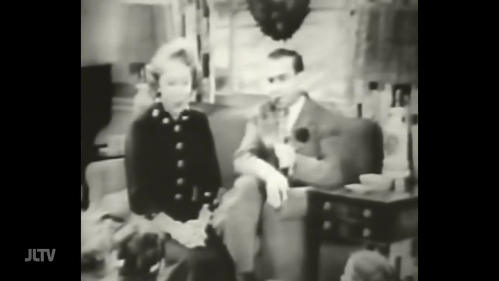 A man and a woman sit side-by-side on a couch, appearing to be on a television show from the United States. The JTLV logo is in the lower left corner of the screen.
