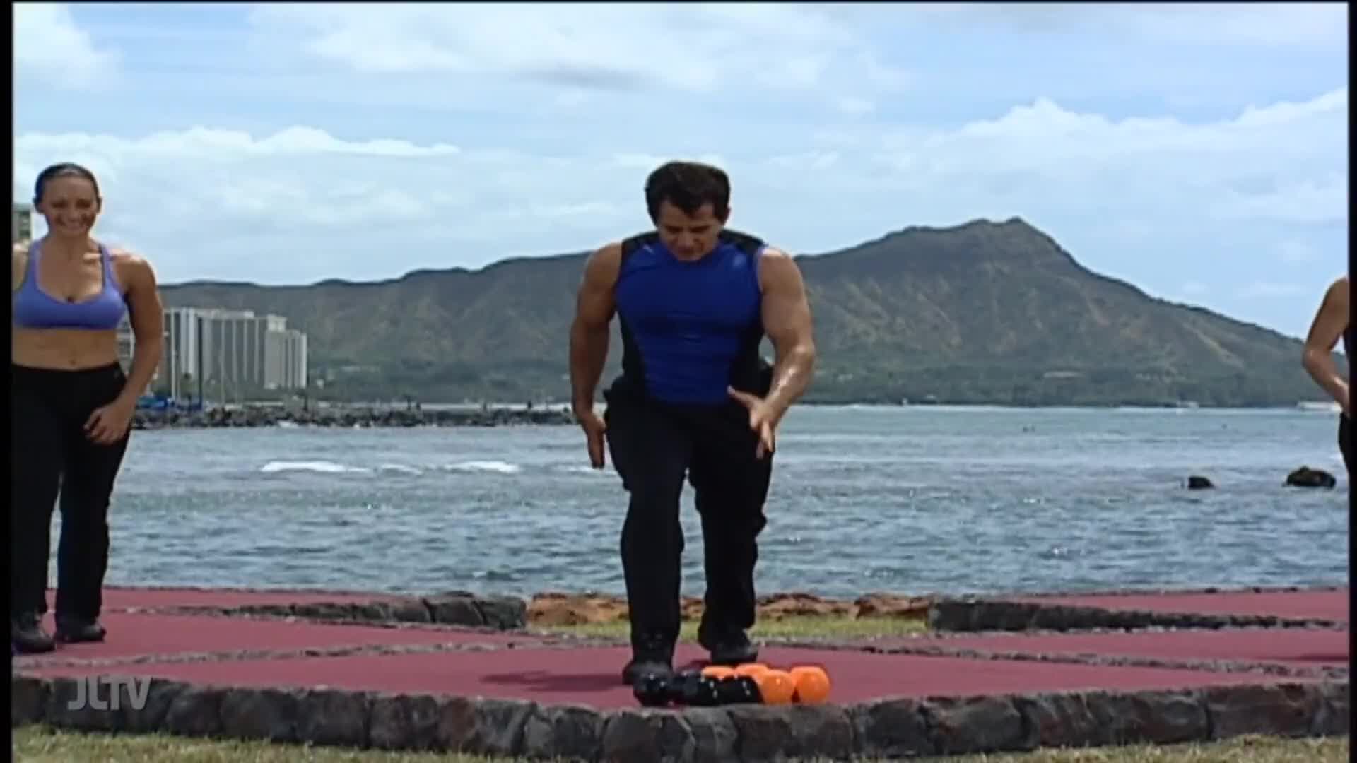 On a sunny day, a man in a blue tank top steps onto a stack of weights. Two other people stand nearby, watching.
