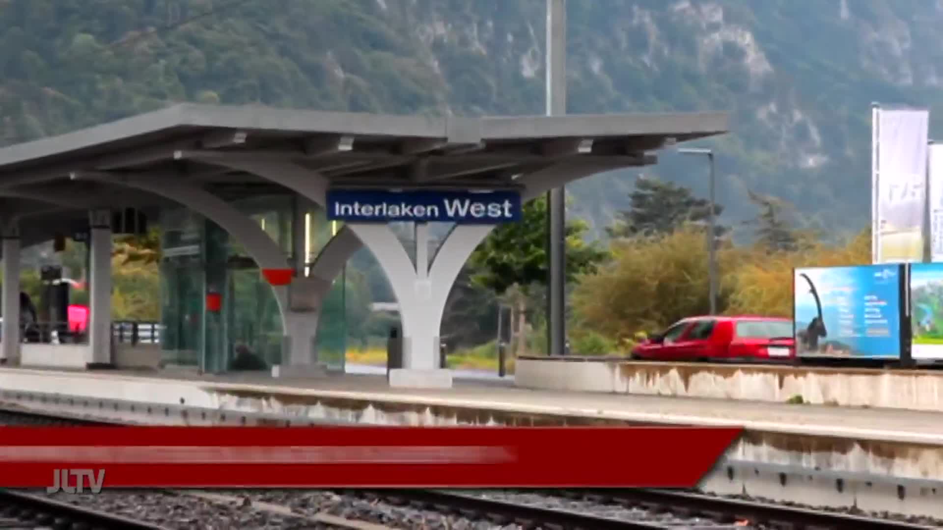 At the Interlaken West station, a red car sits parked near the platform. The scene is framed by a red banner from Jewish Life Television.
