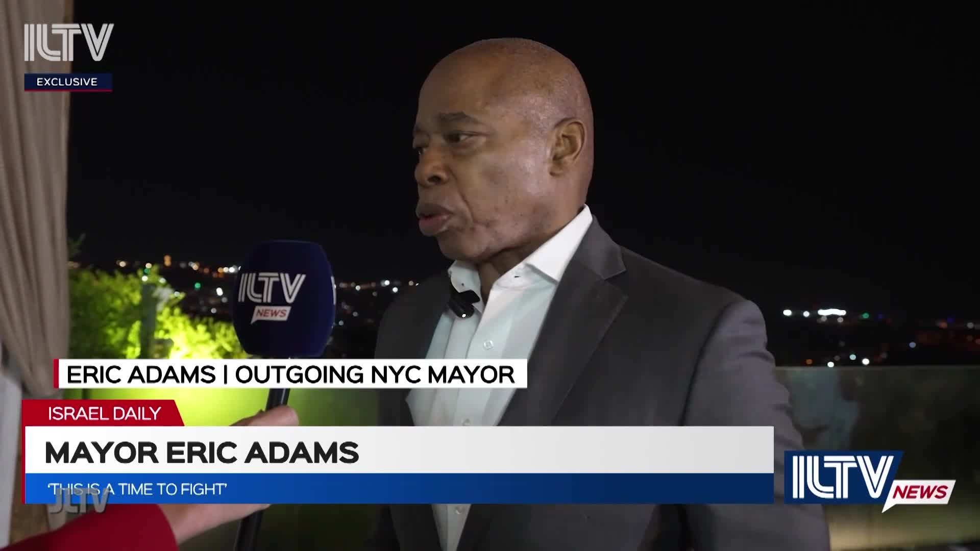 Eric Adams, the outgoing NYC mayor, is speaking into an ILTV microphone. The interview is taking place outdoors at night, with city lights visible in the background.

