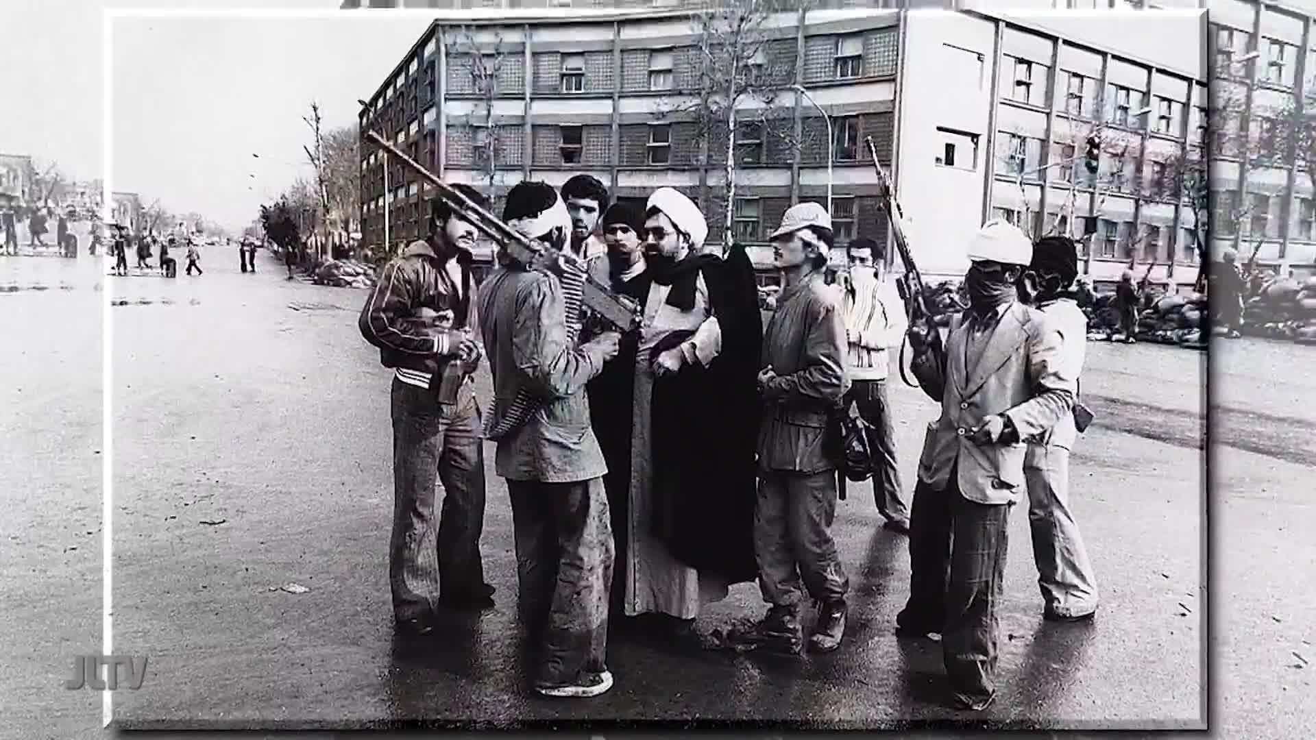 A group of men, some with rifles, surround a robed figure in the middle of a street. The scene, broadcast by United States Jewish Life Television, shows a tense moment.
