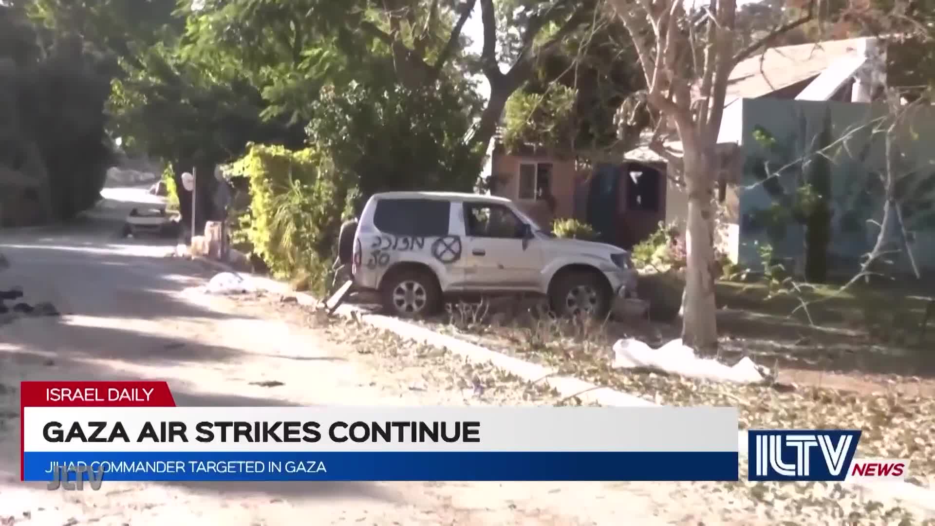 A white SUV, marked with graffiti, sits on the side of a road, debris scattered around it. The scene is being reported on Jewish Life Television, showing the aftermath of apparent air strikes in Gaza.
