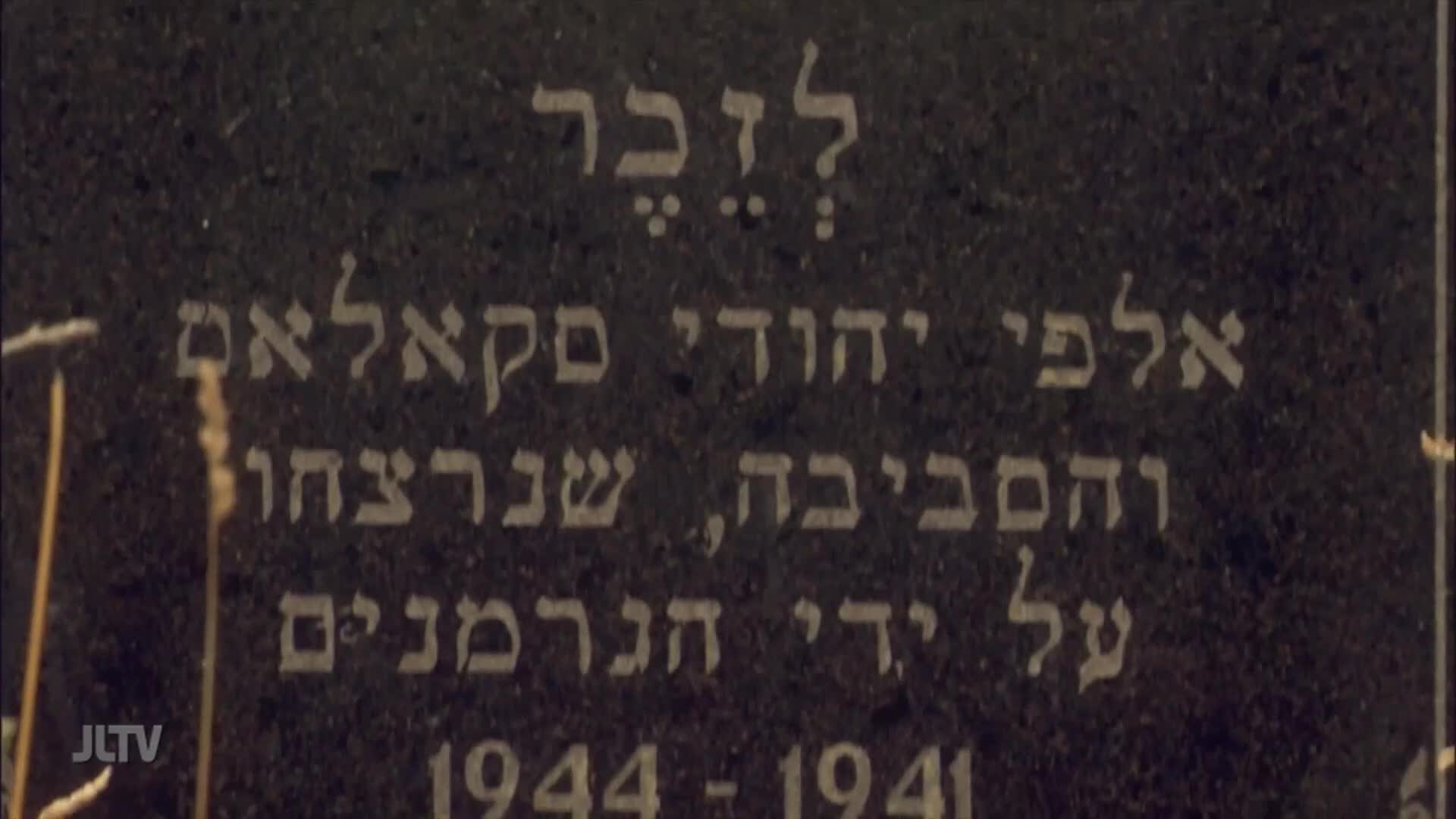 On a dark stone, Hebrew letters are etched, commemorating those murdered by the Nazis. The JLTv logo is visible in the corner, likely from a documentary filmed in the United States.

