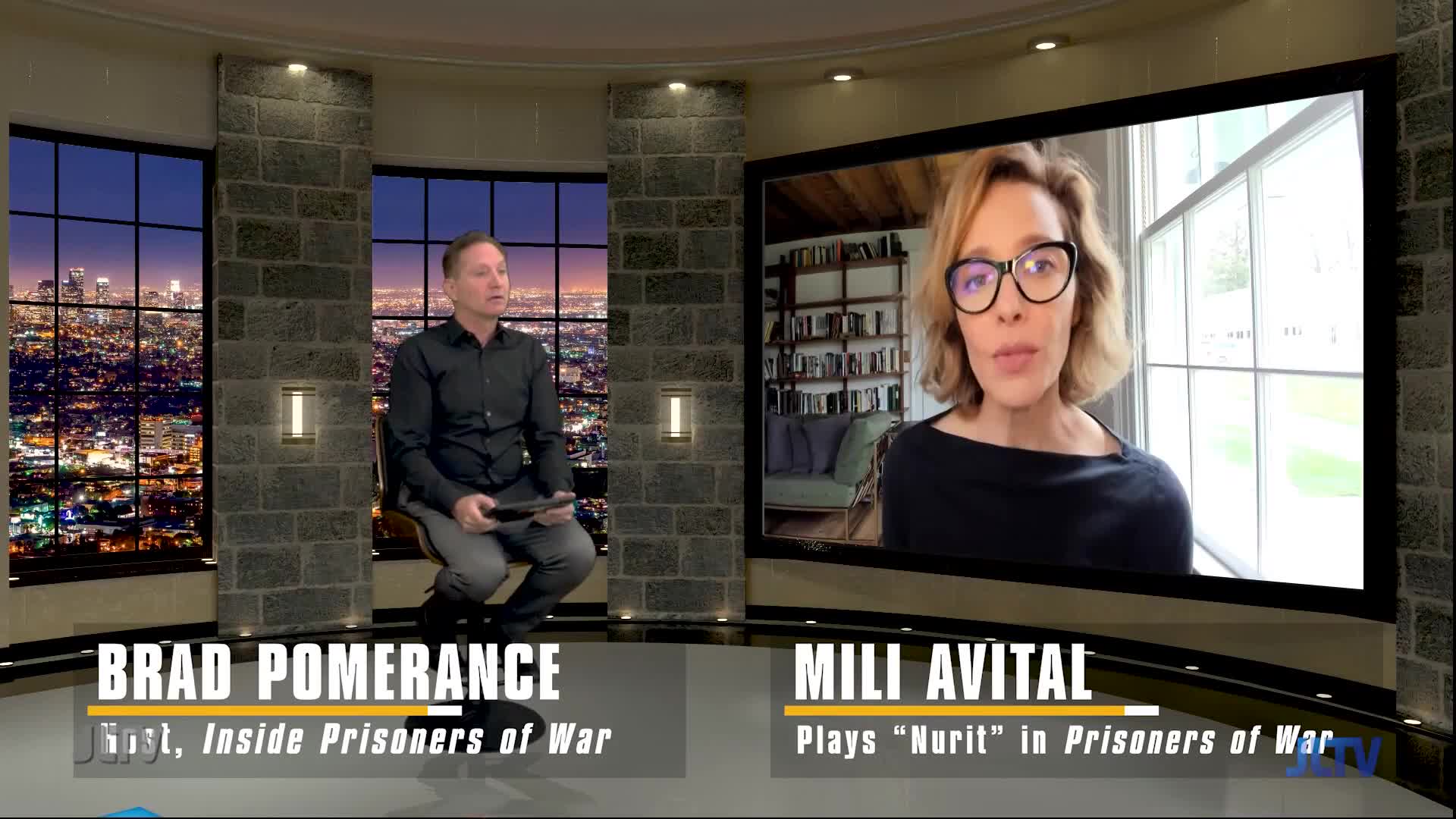 Brad Pomerance, host of "Inside Prisoners of War," sits in a studio with a city skyline behind him. On a large screen, Mili Avital, who plays "Nurit," speaks from a room with bookshelves.
