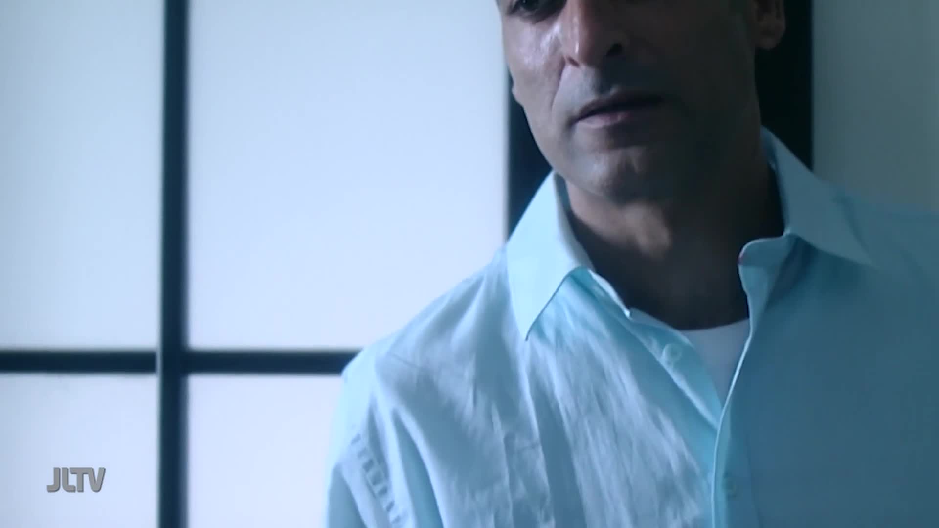 A man in a light blue collared shirt stands in front of a screen with a grid pattern. The JLTV logo appears in the lower left corner.