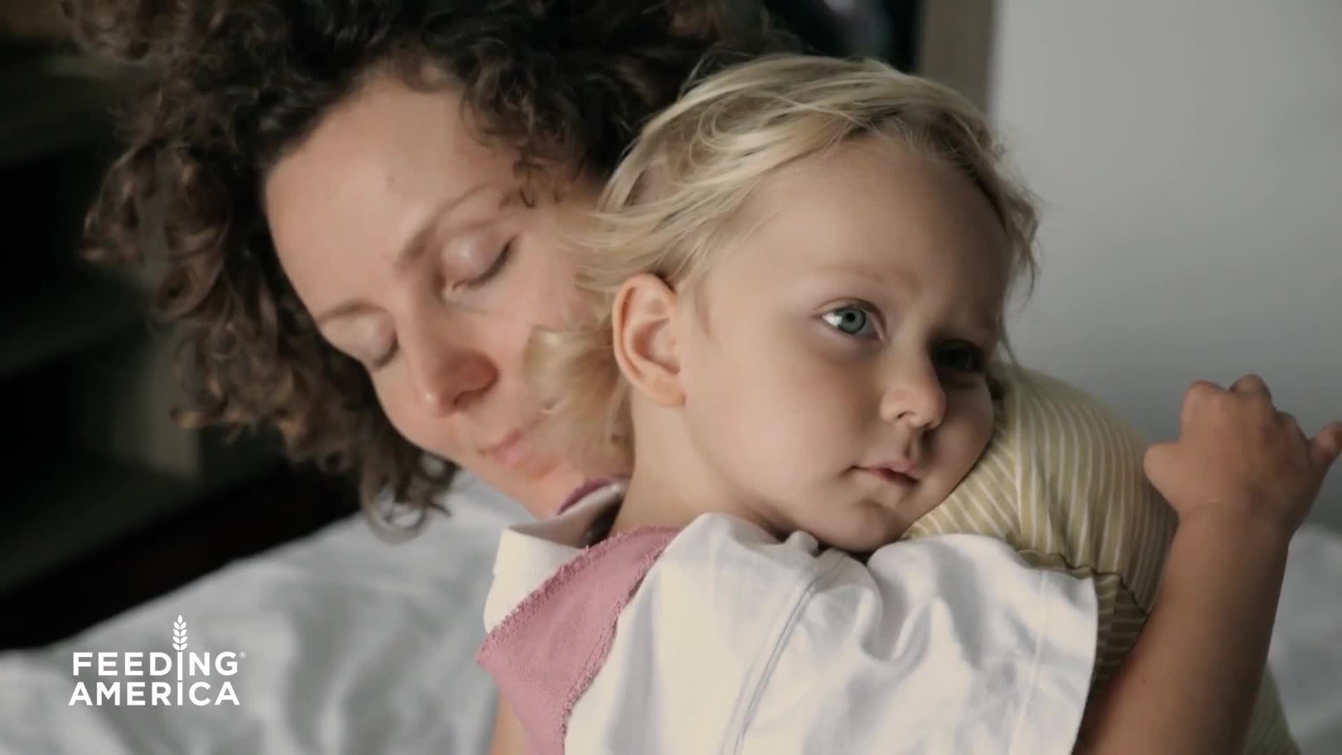 A woman cradles a young child, their faces close. The child's blue eyes gaze forward, while the woman's eyes are closed.