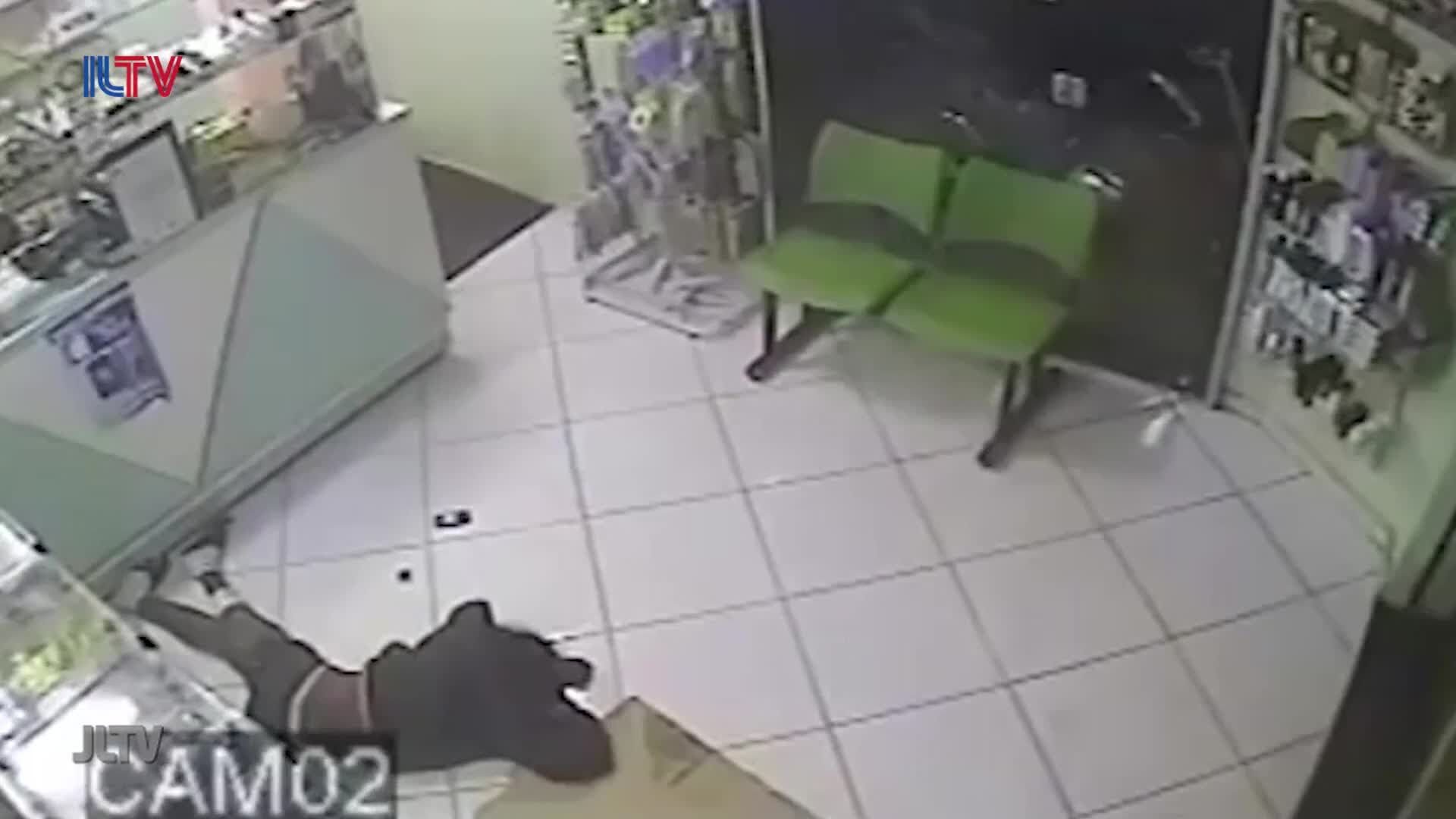 A person in dark clothing lies on the floor, their legs bent and their head turned away. A small, dark object rests near their outstretched arm.