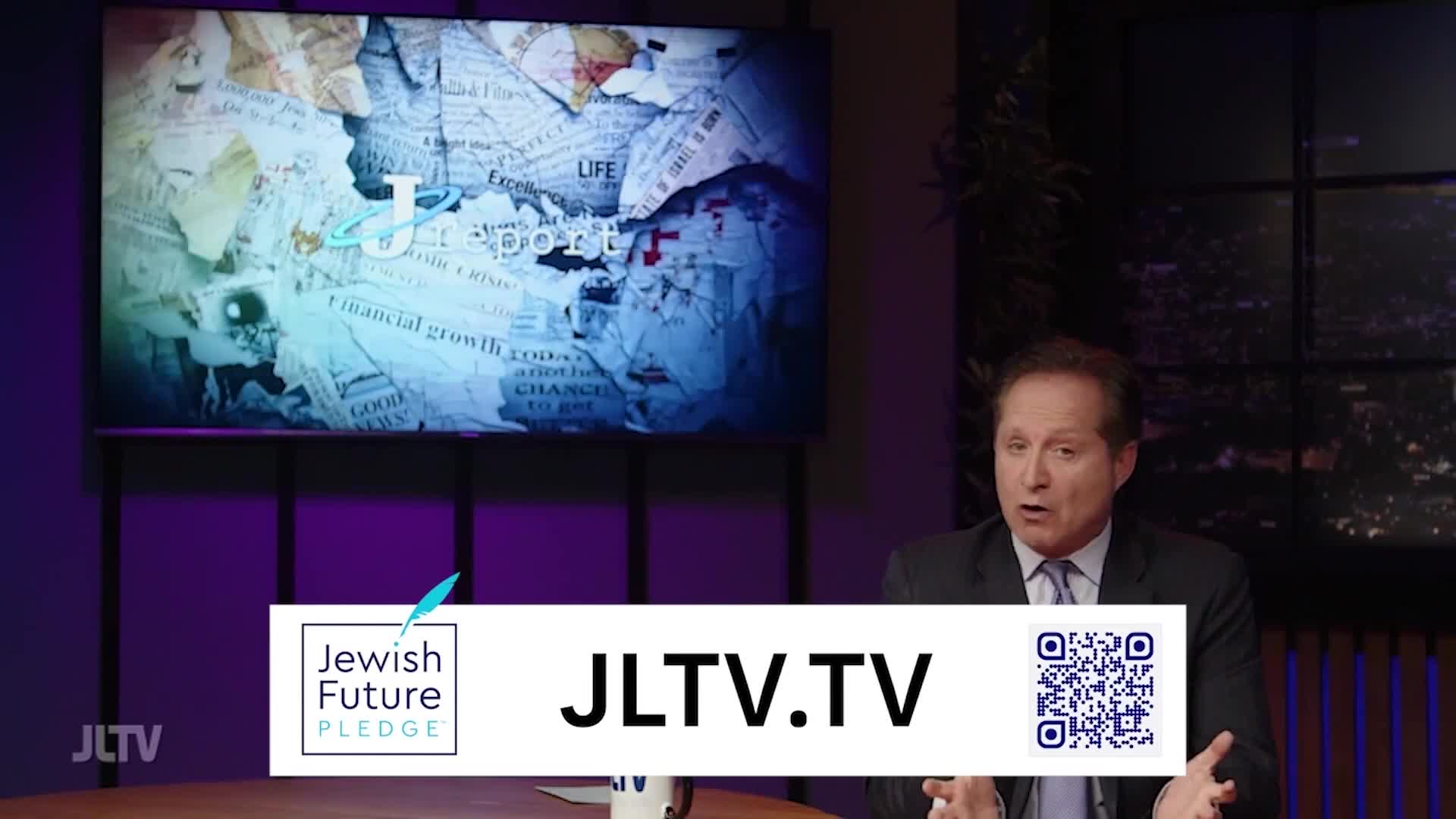 A man in a suit speaks animatedly in front of a screen displaying the JLTV logo and website. The screen behind him shows a collage of newspaper clippings.