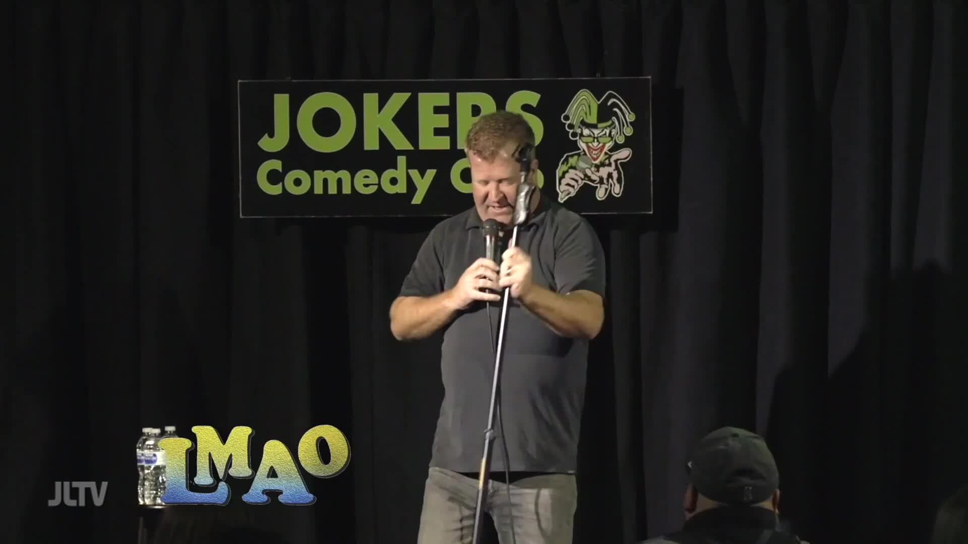 A comedian grips his microphone, his face contorted as he delivers a punchline at Jokers Comedy Club. The JLTV logo and "LMAO" graphic are visible in the foreground.