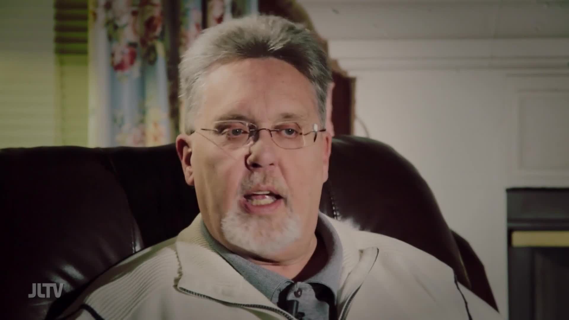 A man with glasses and a gray beard speaks from a dark leather chair. The JLTV logo appears in the lower left corner.