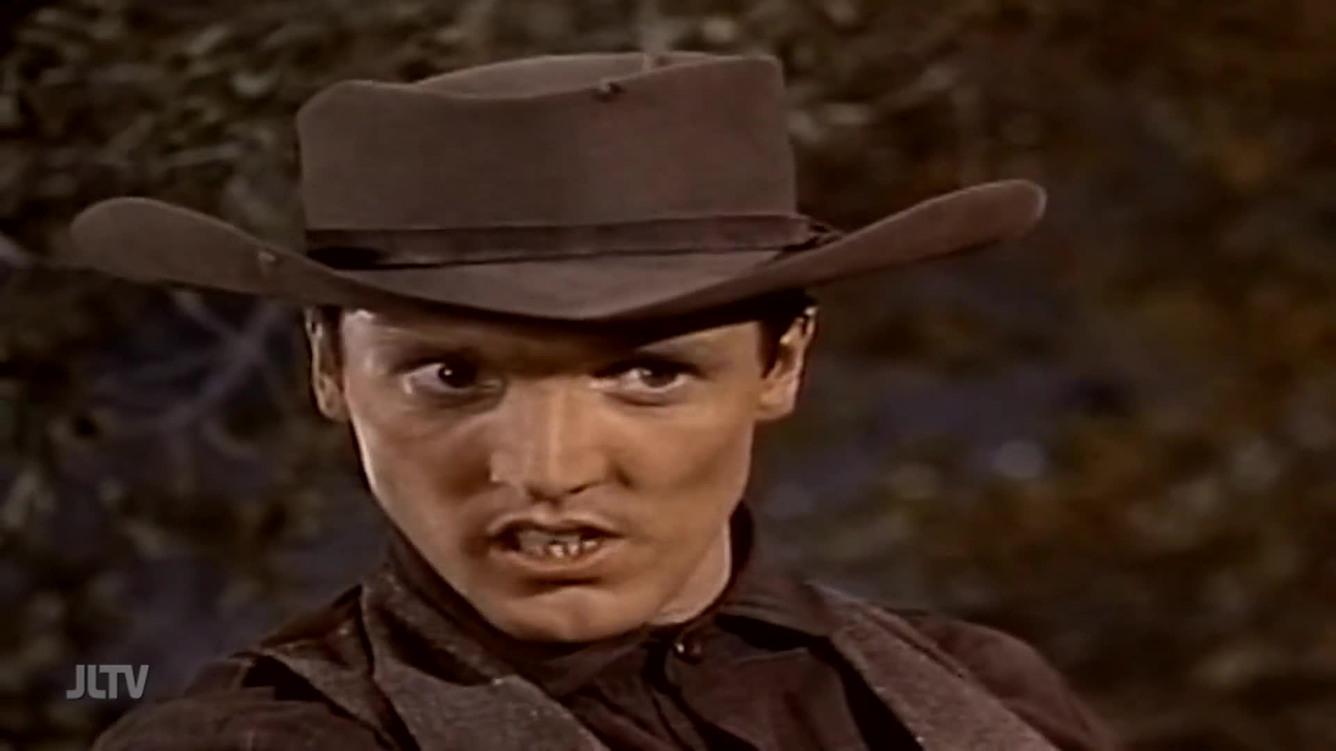 A man in a cowboy hat glares intensely, his teeth bared in a snarl. He looks ready for a confrontation, his eyes fixed on something just out of frame.
