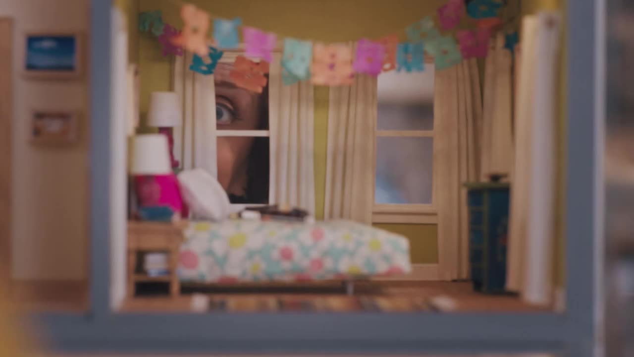 A wide, startled eye peers in from the window, framed by a miniature bedroom. The eye is the focus, the rest of the room a blur with a bed, lamps, and colorful decorations.
