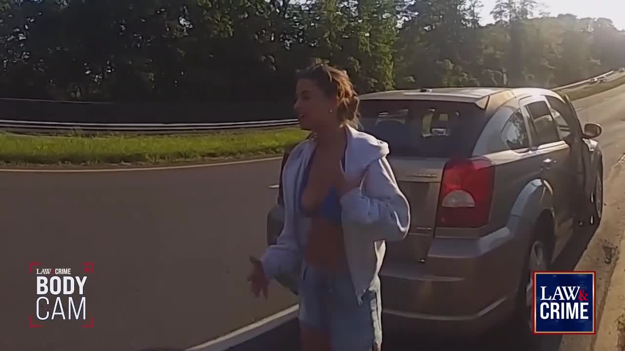 A woman stands next to a parked car on the side of a highway, gesturing with her hands. The "Law & Crime" logo is visible in the corner, suggesting this is body cam footage.
