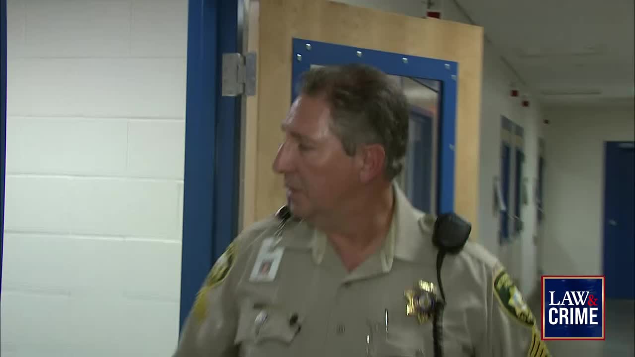A uniformed man walks through a doorway, looking to his left. The Law & Crime logo sits in the corner, suggesting this is a scene from a United States legal program.
