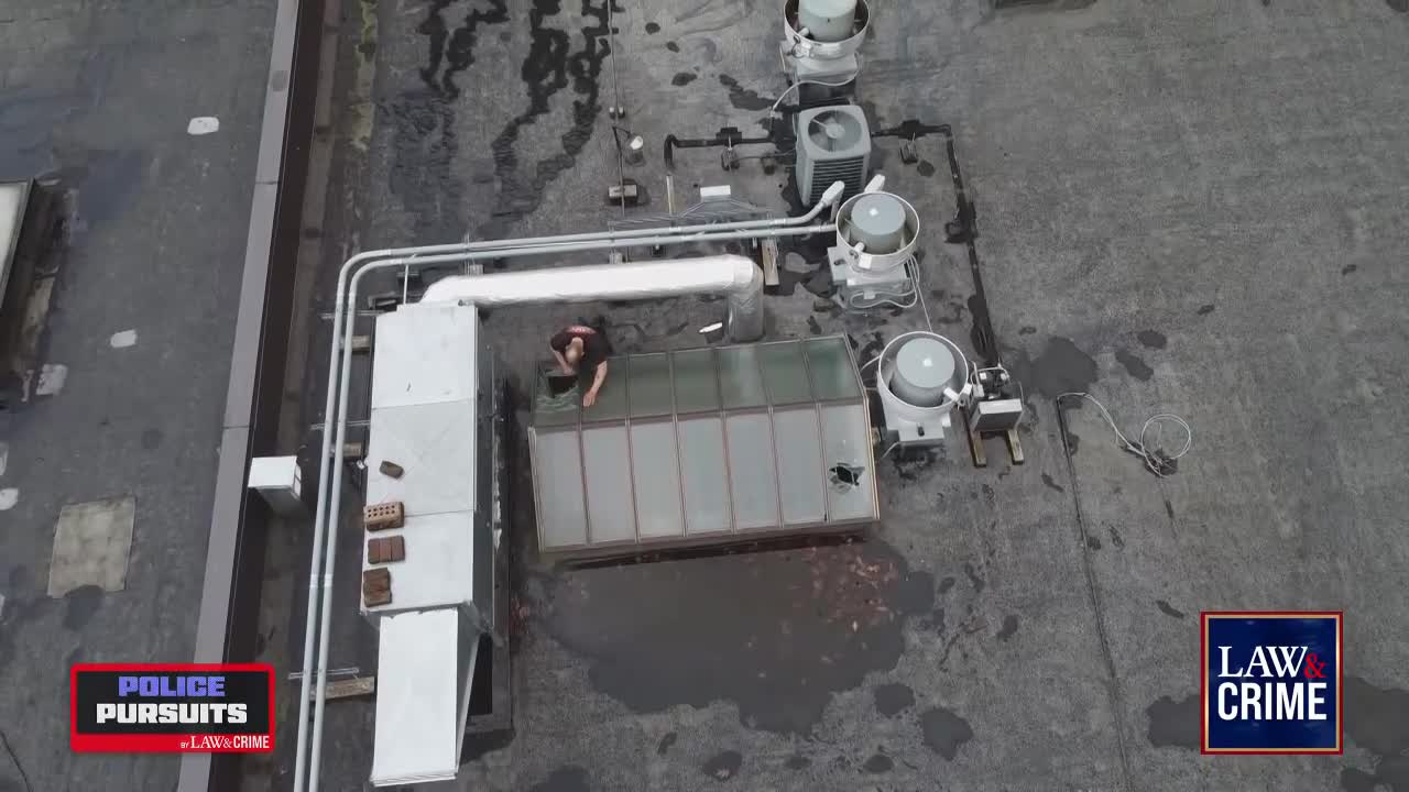 A person is crouched on a rooftop, near a water-filled puddle, seemingly inspecting a damaged skylight. The scene is part of a Law & Crime segment about police pursuits.

