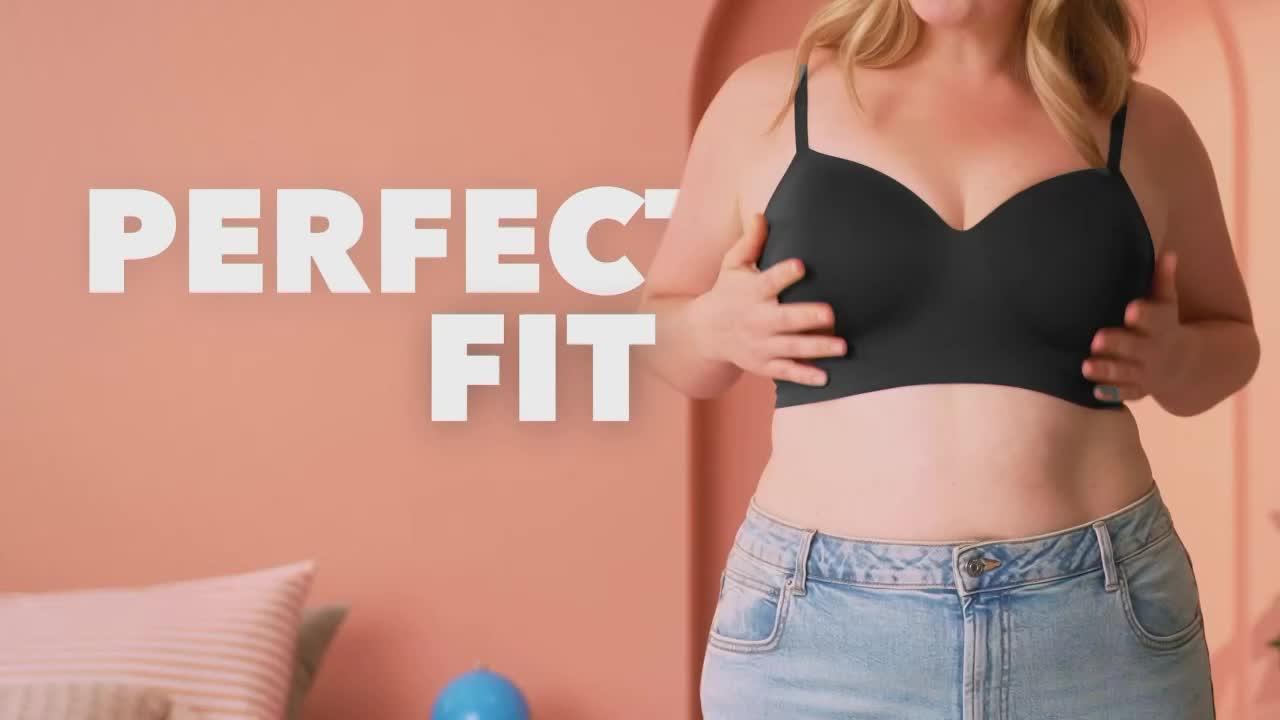 A woman in a black bra and jeans holds her hands up, cupping her breasts. Bold white letters spell out "PERFECT FIT" against a pink backdrop.
