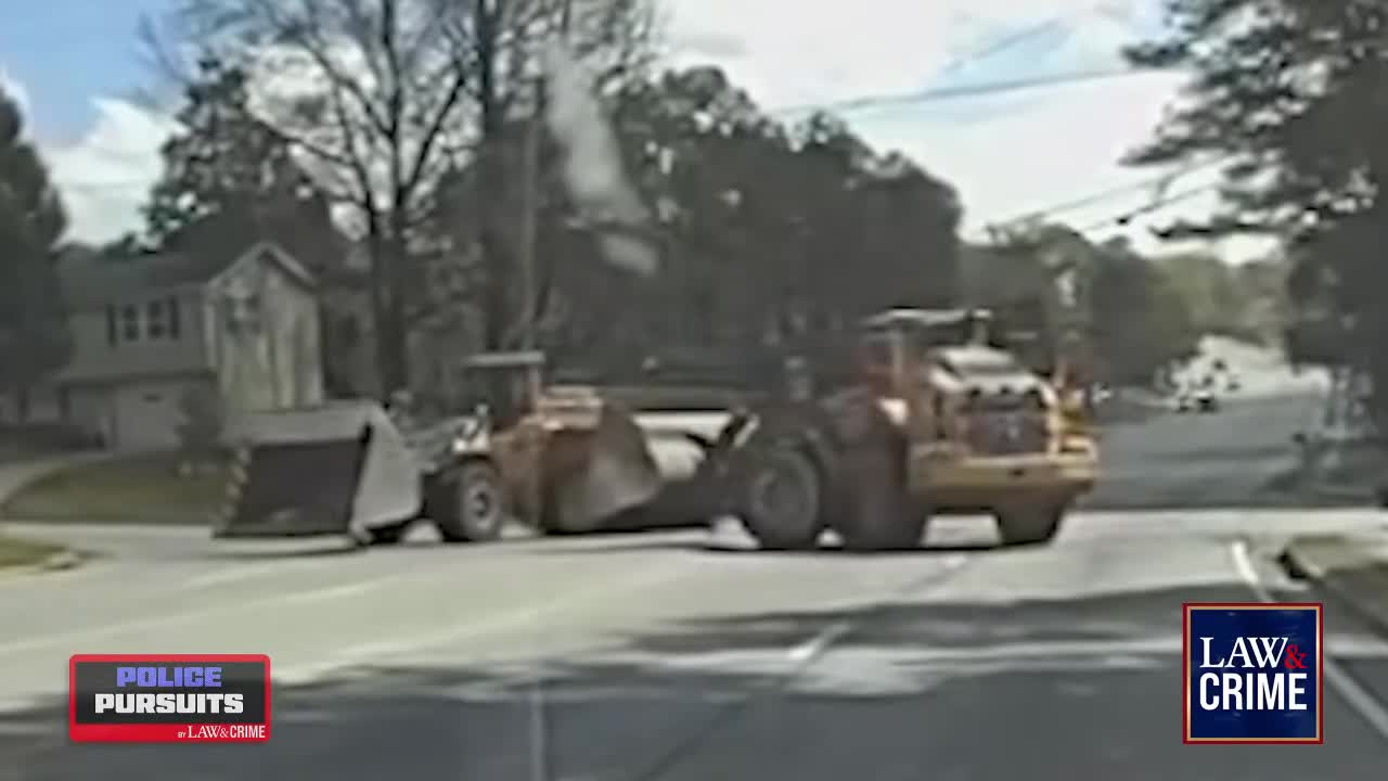 Two large, orange construction vehicles are positioned across a road intersection. Steam rises from one of them, likely from the engine.
