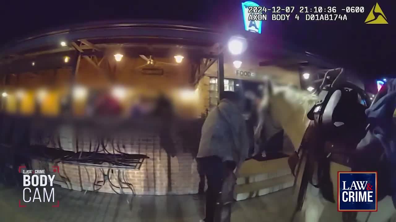 Outside a restaurant, a person in a gray jacket leans forward, interacting with others near the entrance. The scene is captured by a body cam, as indicated by the "Law & Crime" logo.
