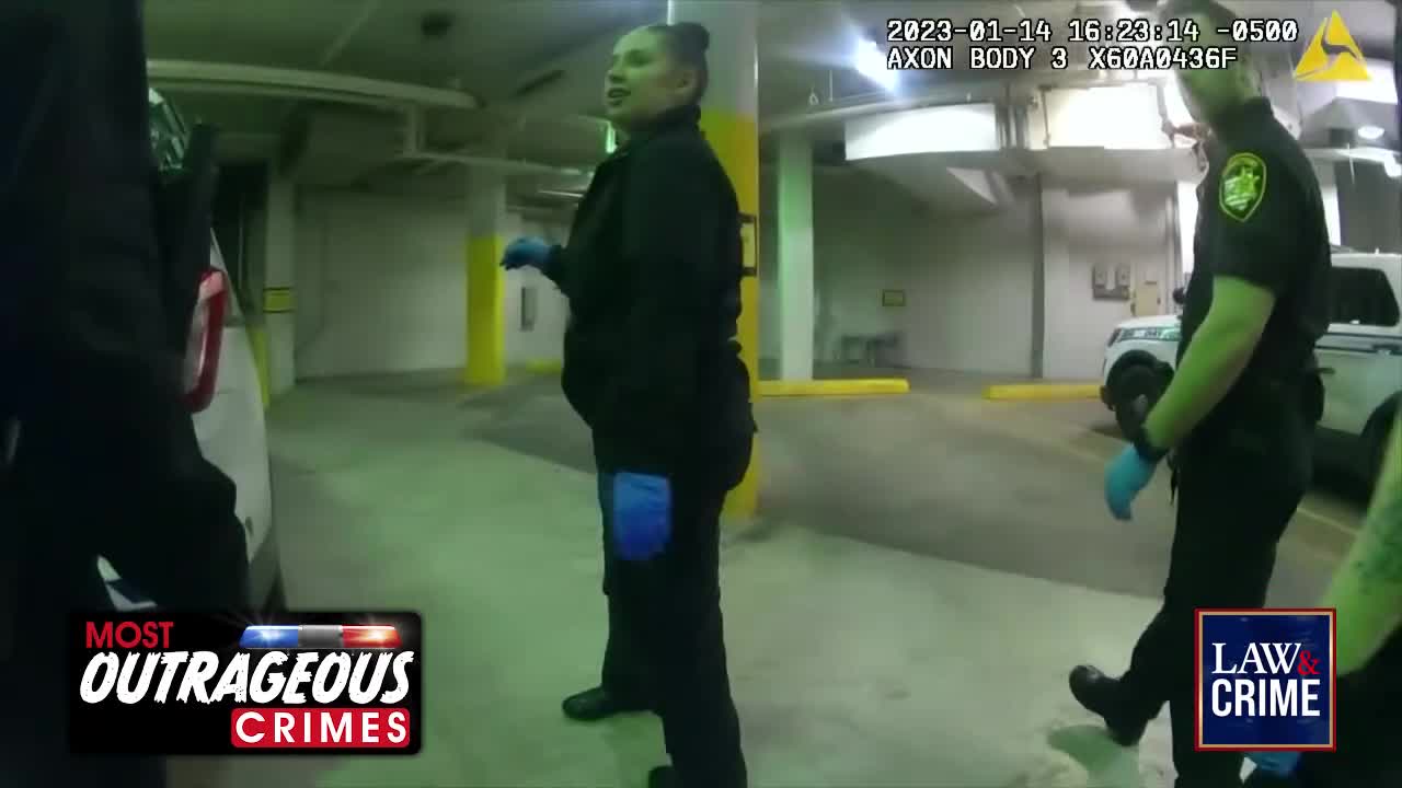 Two officers, wearing blue gloves, are in a parking garage; one is speaking and gesturing while the other walks towards a police car. The scene is being recorded, as indicated by the "AXON BODY" timestamp.
