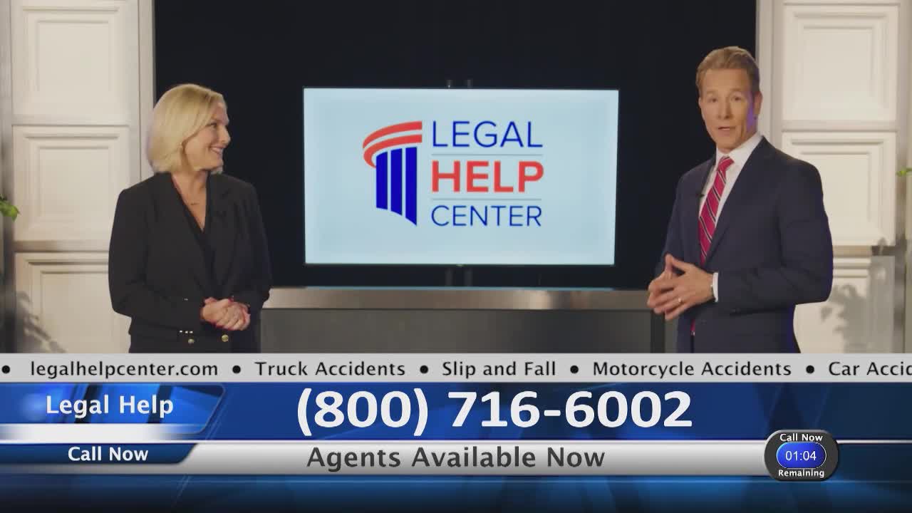 A man in a suit gestures while speaking, and a woman in a black blazer stands beside him, smiling. The backdrop features a logo for "Legal Help Center" and a phone number.
