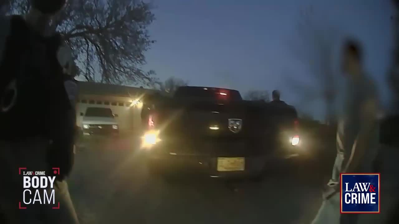 A black pickup truck sits on a residential street, its brake lights illuminated. Two figures stand near the vehicle, likely in the context of a Law & Crime body cam clip.
