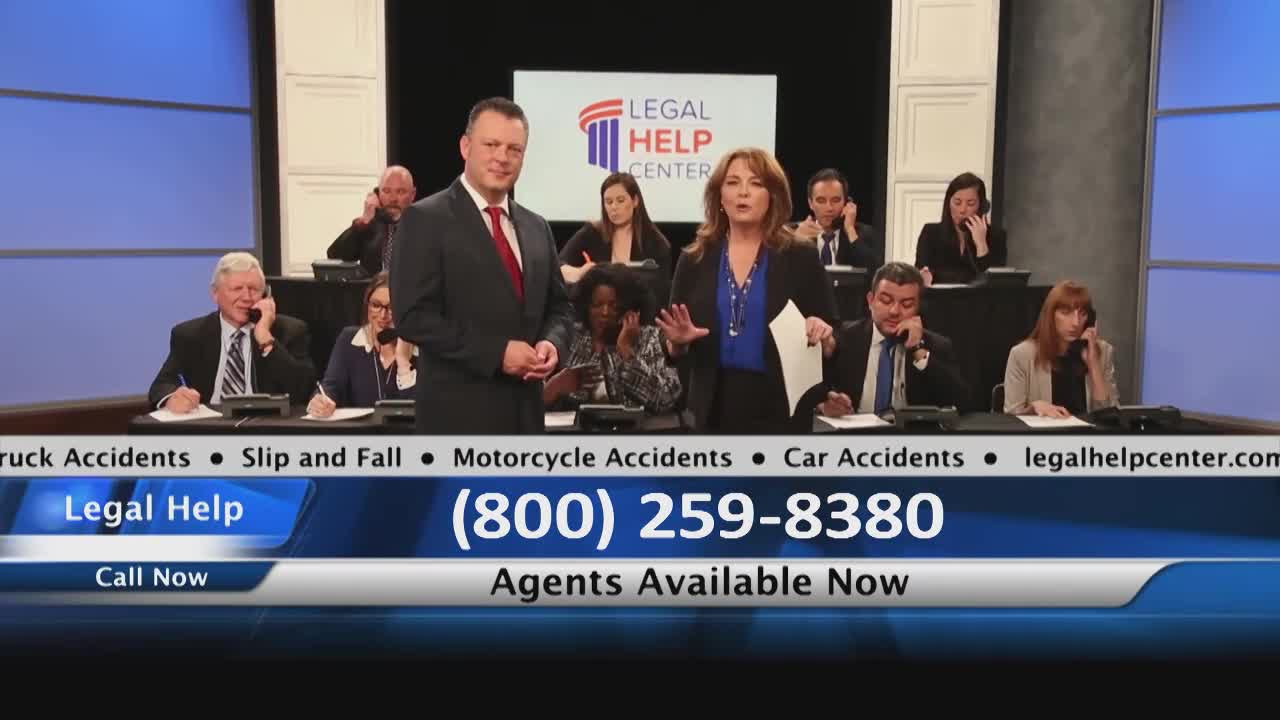 A man and a woman stand in front of a backdrop, gesturing towards the camera. Behind them, several people are seated at desks, talking on phones, presumably taking calls for "Legal Help."
