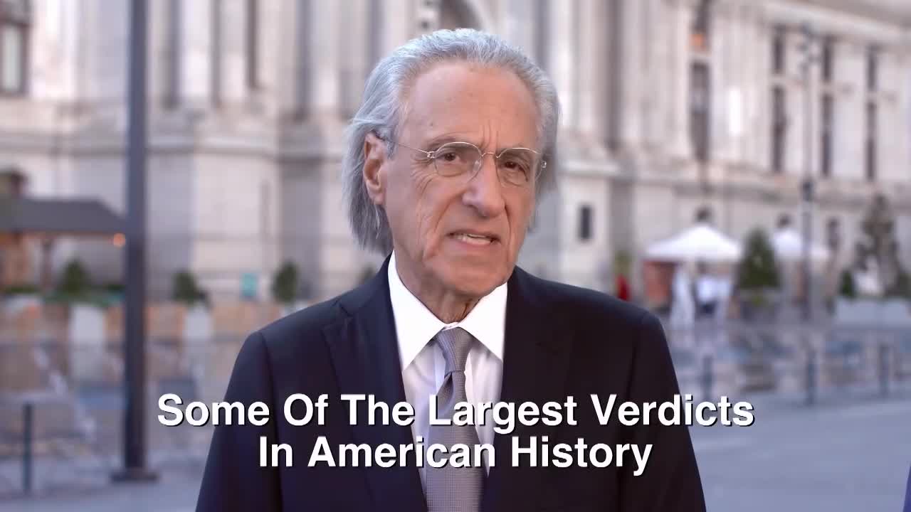 A man in a suit and tie, framed against a blurred city backdrop, speaks directly to the camera. Text on the screen announces, "Some Of The Largest Verdicts In American History."
