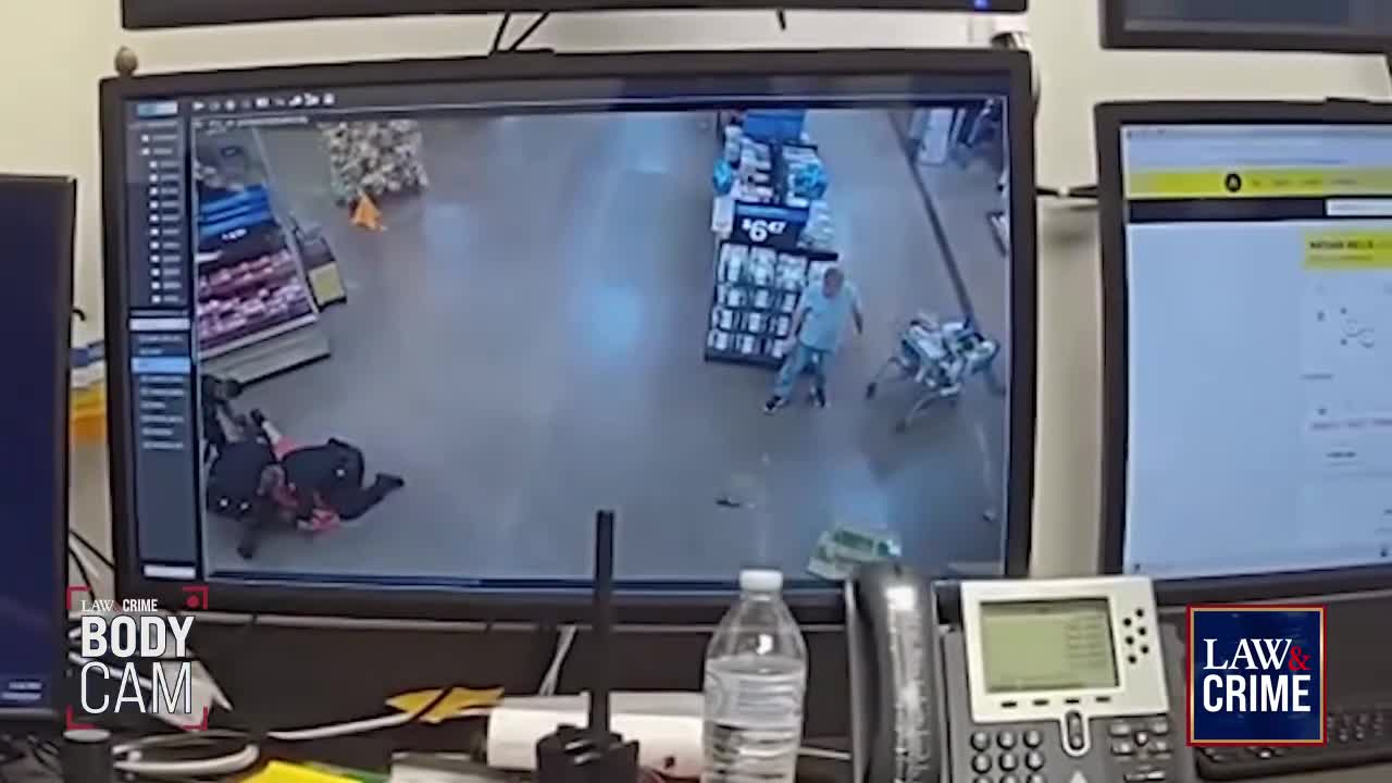 A man in a light blue shirt is on the ground, struggling with two individuals in dark clothing. Nearby, another person is on their hands and knees.