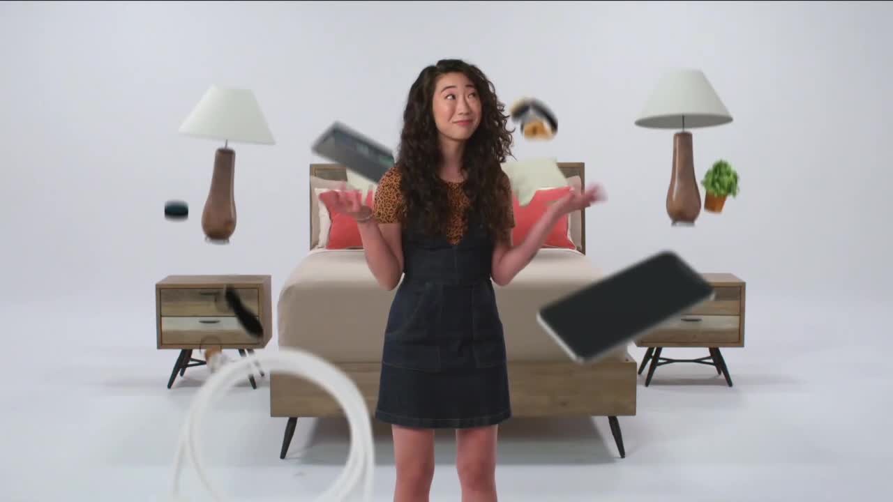A young woman stands with her hands outstretched as various objects, including lamps, phones, and a small plant, hover around her. The scene unfolds like a surreal moment, perhaps from a courtroom dramatization where evidence is presented in an unusual way.