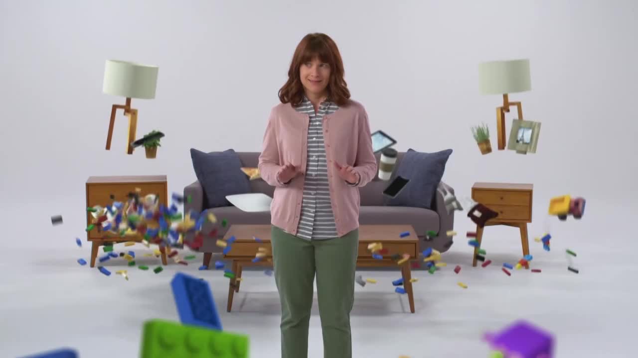 A woman stands amidst a chaotic scene where furniture and toys are suspended in mid-air. Building blocks scatter around her, some tumbling from a nightstand and others already on the floor.
