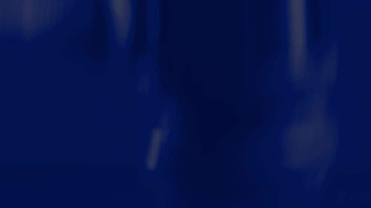 A figure in a light-colored shirt stands at a podium, illuminated by a spotlight. The background is a deep, dark blue, suggesting a formal setting like a courtroom or press conference.