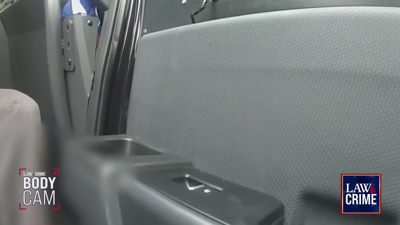 A blue and white shirt is visible through a gap in the vehicle's interior. The camera is positioned low, looking up at the textured seat and a metal partition.