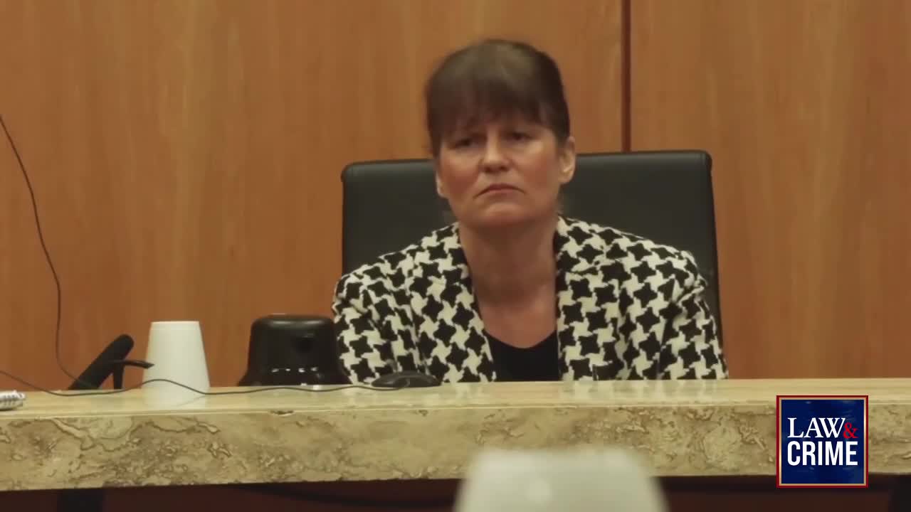 A woman in a black and white patterned jacket sits at a table in a courtroom. A "Law & Crime" logo appears in the lower right corner.