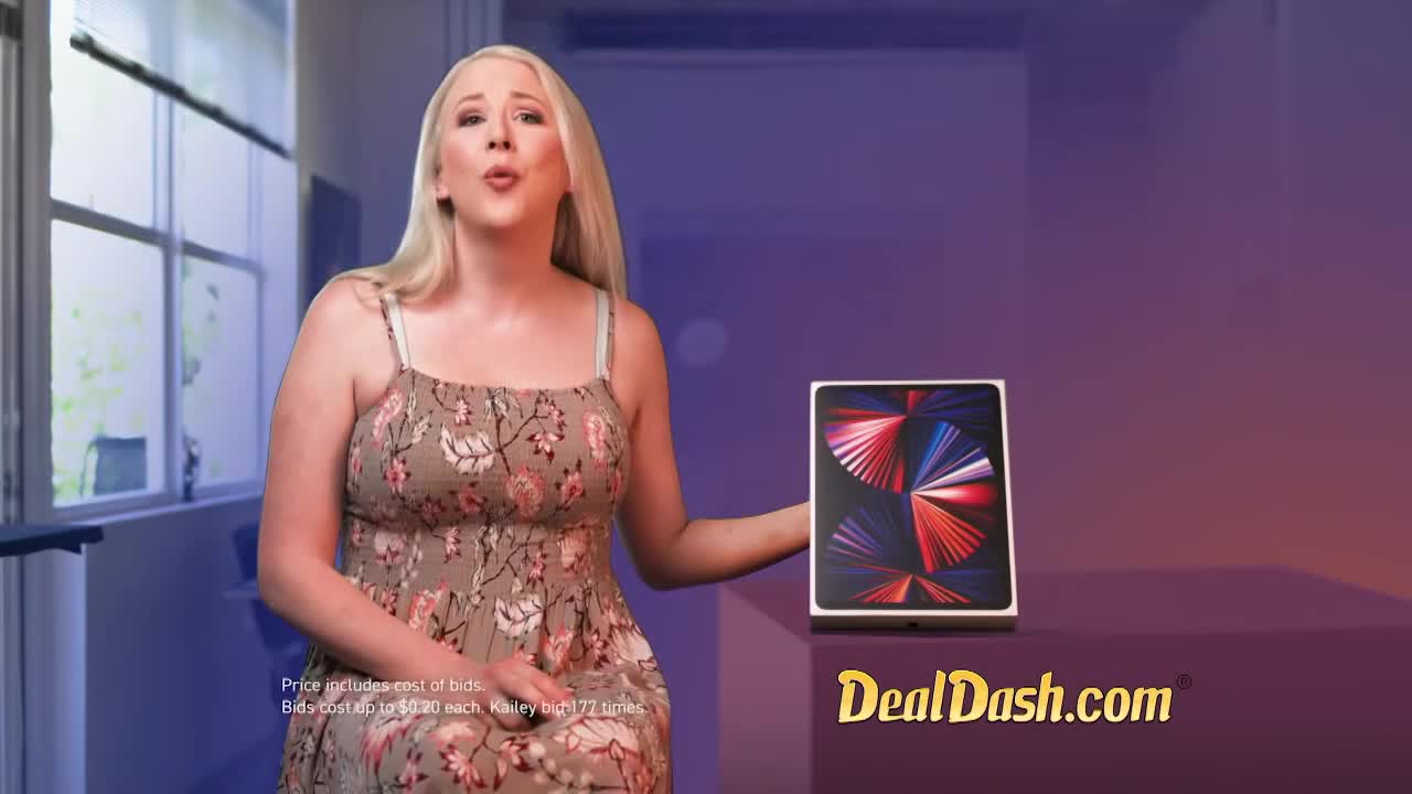 A woman in a floral dress holds up a new iPad. The DealDash.com logo appears on screen.