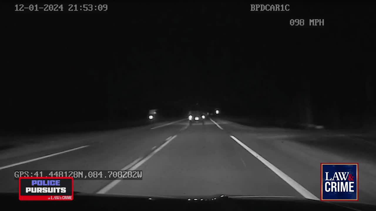 The car ahead is speeding down a dark highway, its taillights a distant glow. The speedometer reads 98 miles per hour, indicating a high-speed pursuit is underway.