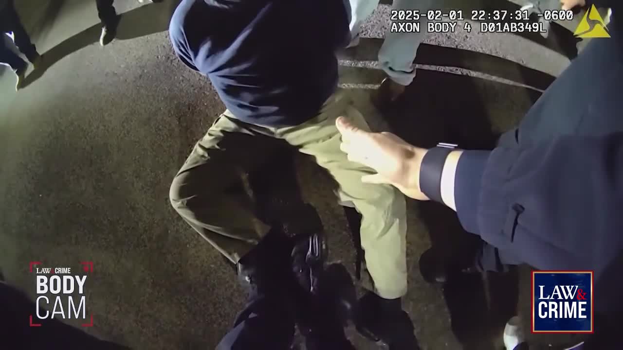 Officers are holding down a man on the asphalt. A hand in a dark uniform sleeve grips the man's thigh.