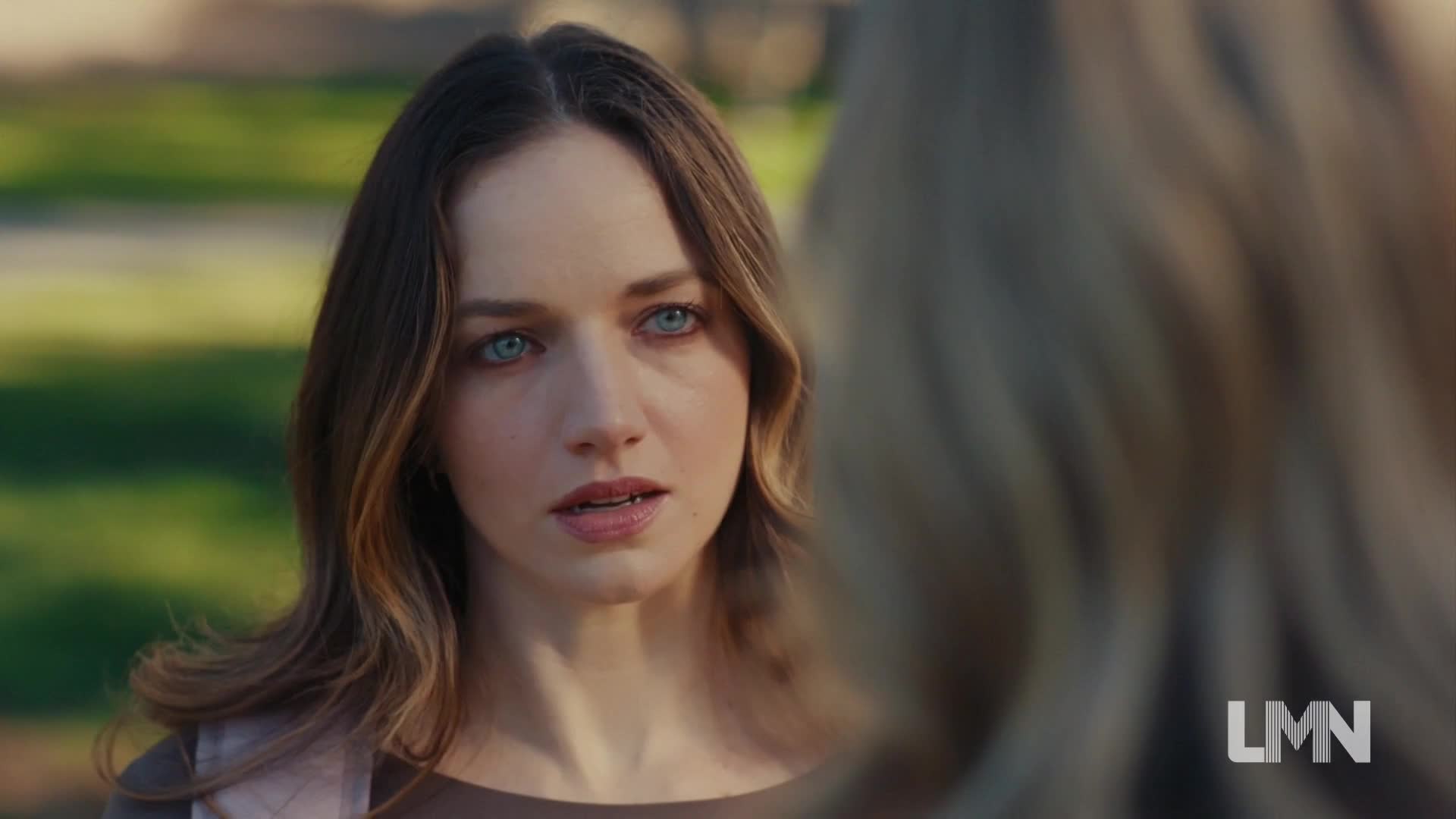 A woman with striking blue eyes stares intently, her lips slightly parted. Her expression suggests worry as she listens to someone off-screen, likely in a scene from a Lifetime movie.
