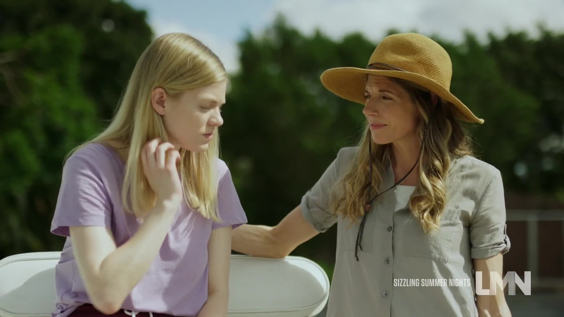 A woman in a straw hat comforts a younger woman, touching her arm. The blonde girl in a purple shirt looks down, scratching her neck.
