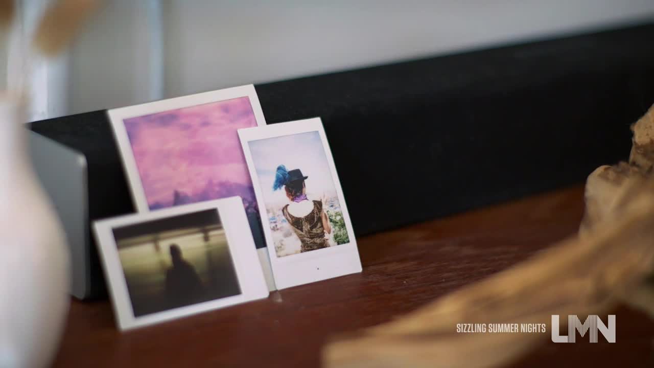 Three faded Polaroid photos lean against a black speaker on a wooden surface. One shows a figure with a hat and blue feathers, another a silhouette, and the third a purple sky.
