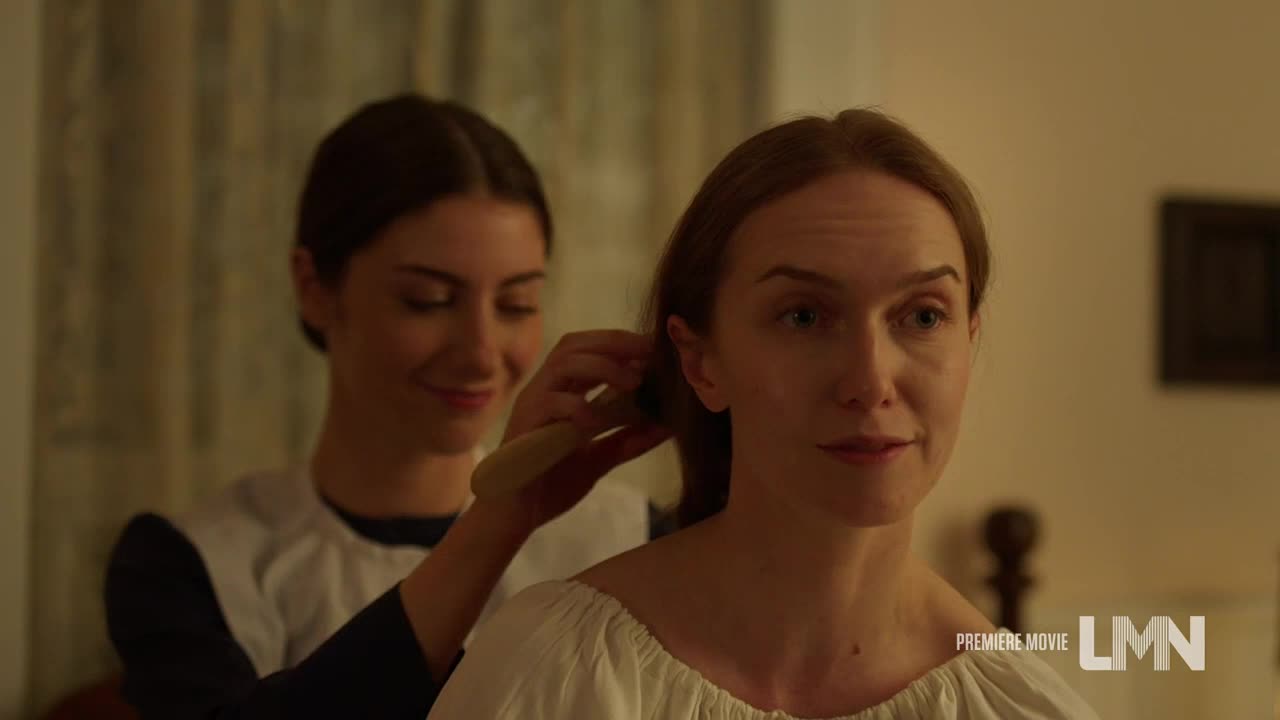 A woman in a white blouse sits, while another, wearing a maid's uniform, gently brushes her hair. The scene is softly lit, and both women appear calm.
