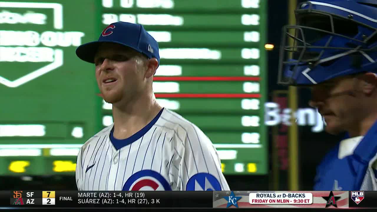 The Chicago Cubs player, with sweat glistening on his face, looks on with a slight grimace. Beside him, a catcher in blue gear stands, his face partially obscured by his mask.
