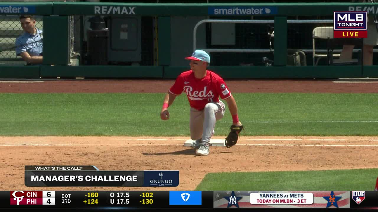 A Cincinnati Reds player in a red jersey is down on one knee, glove in hand, near a base. The MLB Tonight graphic shows a manager's challenge is underway.
