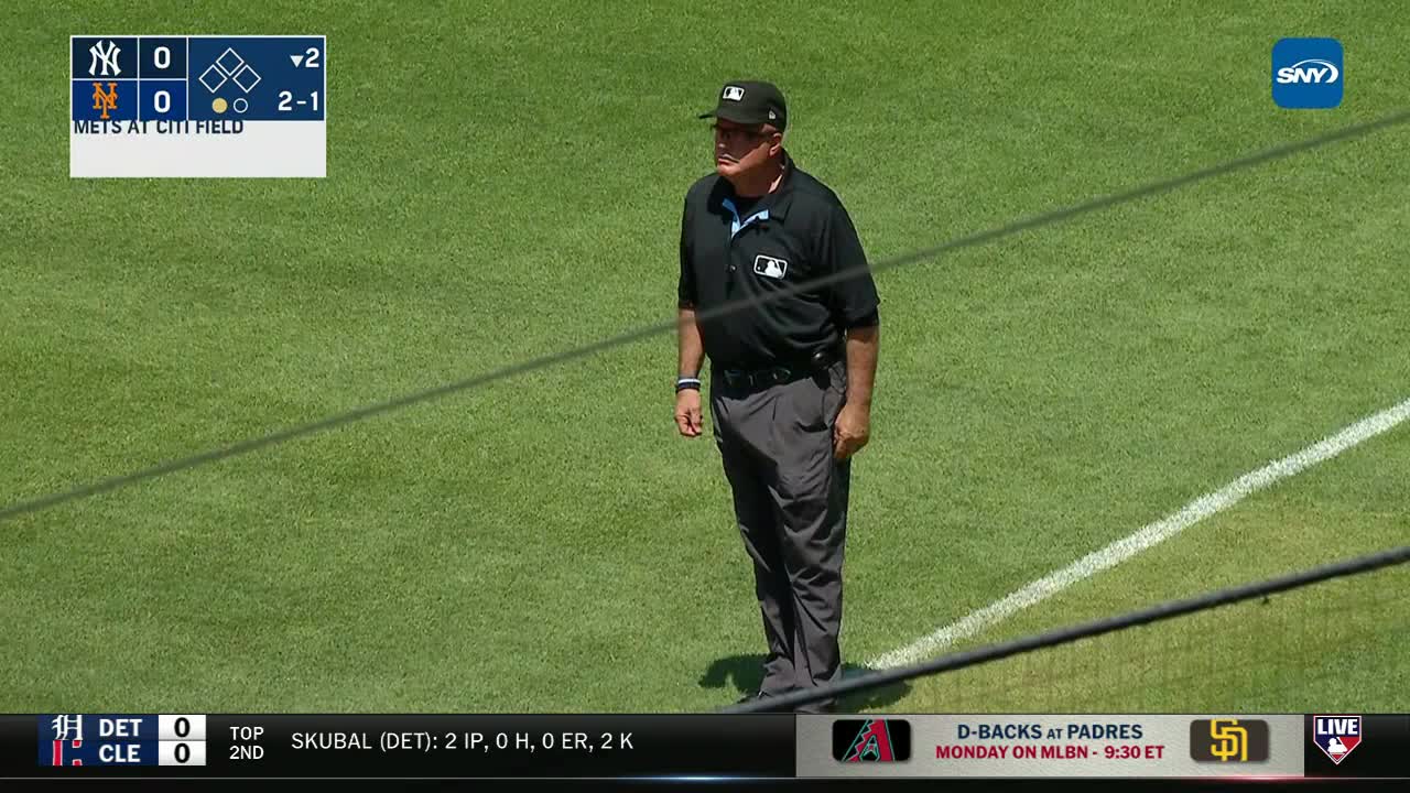 An umpire, dressed in black, stands at attention on the field. The scoreboard indicates a game between the Yankees and Mets at Citi Field, on MLB Network.
