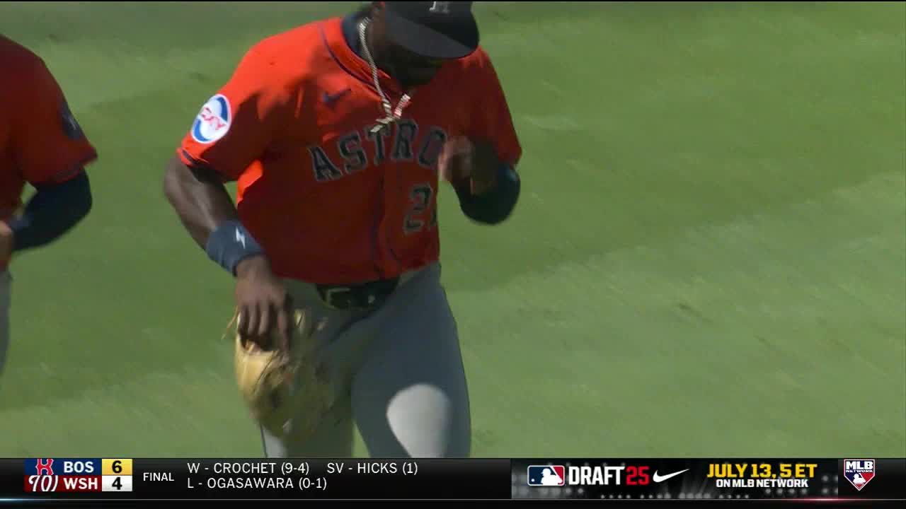 The Astros player in the orange jersey is walking, glove in hand. He's looking down as he moves across the green field, the MLB Network logo visible in the corner.
