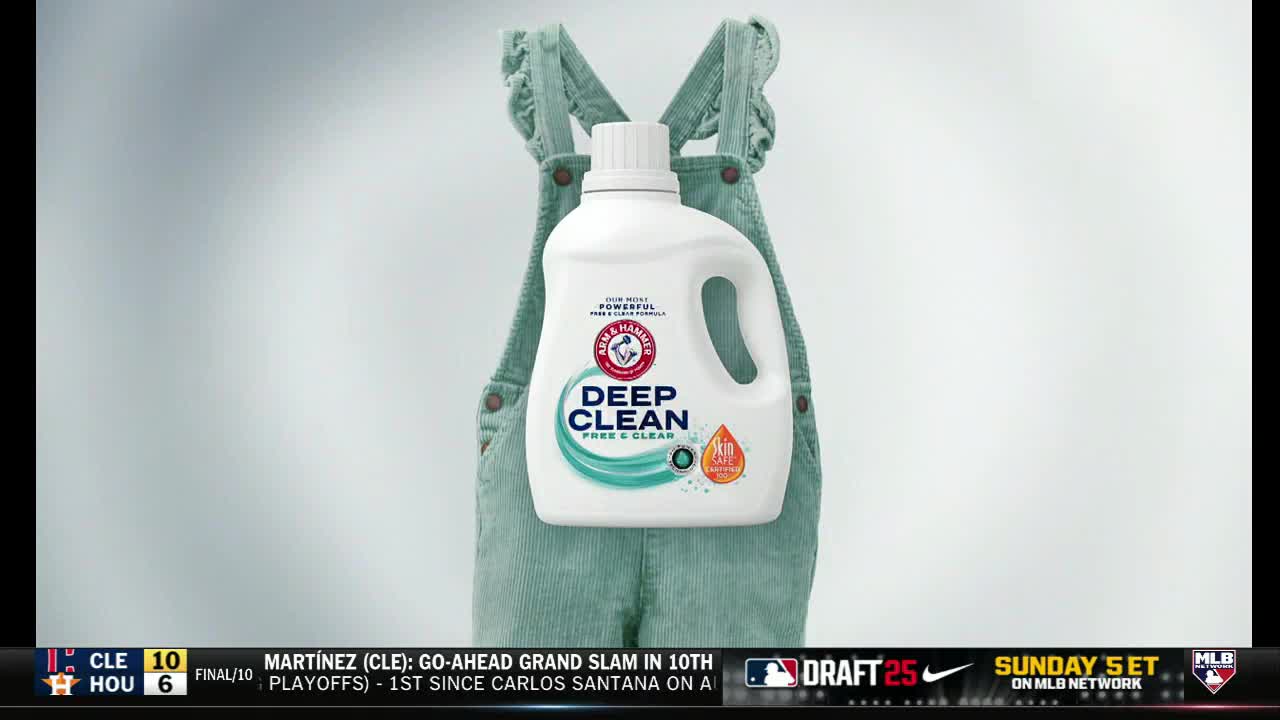 A bottle of laundry detergent is centered, propped up against a pair of corduroy overalls. The MLB Network logo and game scores are visible at the bottom of the screen.
