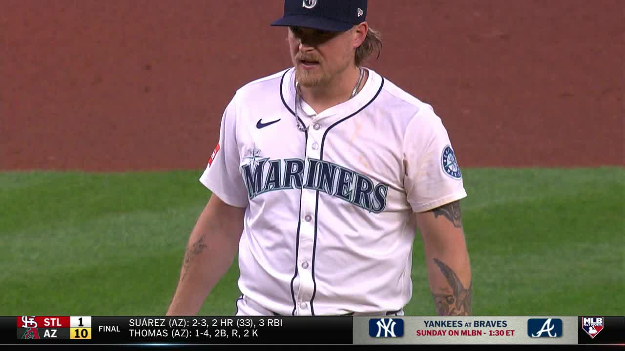 The Seattle Mariners pitcher stands on the field, looking down. His jersey is white, and the word "Mariners" is across his chest.
