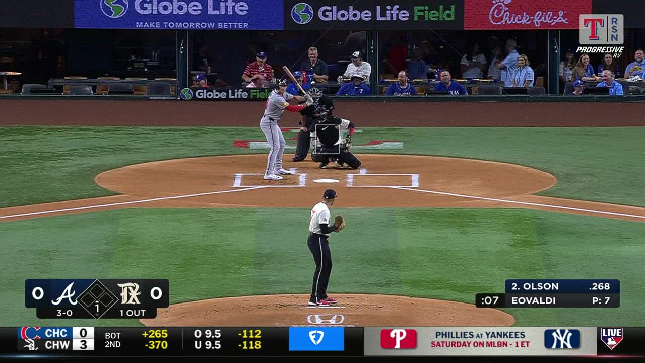 The pitcher, in a white jersey, is poised to throw. The batter, wearing a red and gray uniform, is ready to swing at the plate.
