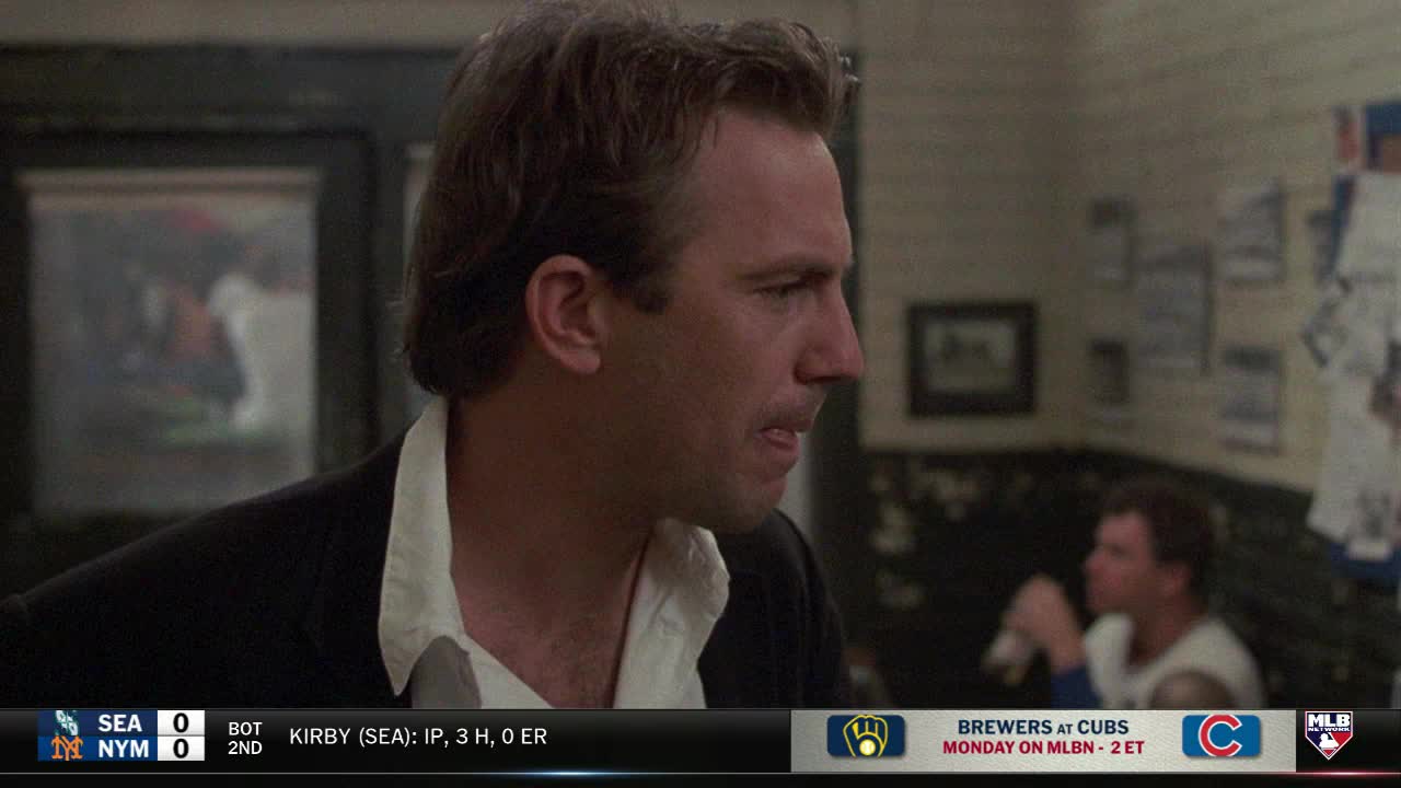 A man in a black jacket and open white shirt is talking, his expression intense. MLB Network's bottom banner shows a baseball game score and a Brewers at Cubs preview.
